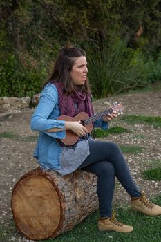 young brunette girl with long hair playing ukulele in the field on the grass