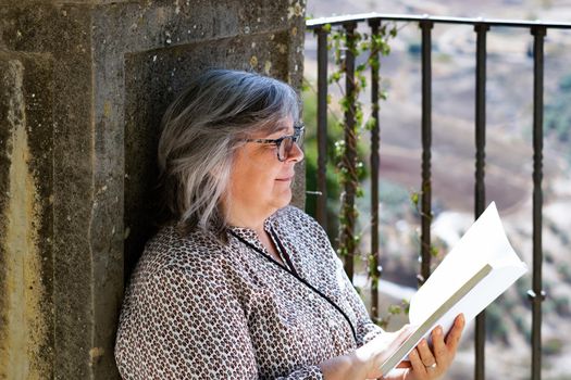 white-haired woman with glasses reading a book in the park