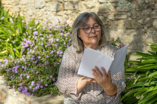 white-haired woman with glasses reading a book in the park