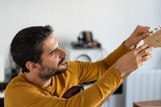 young boy with beard playing guitar at home with piano on the back