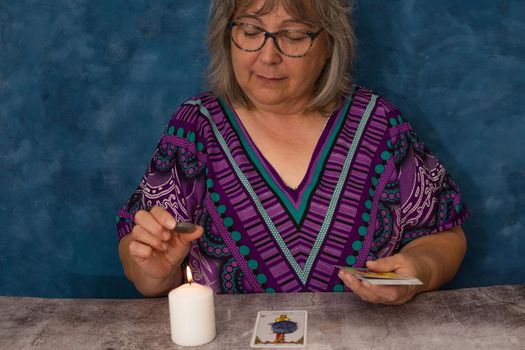 older white-haired woman reading tarot cards on a wooden table with candle