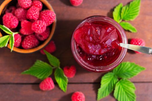 fresh raspberry jam in a glass jar on a wooden table, next to fresh raspberries. concept of homemade jam, preserves for winter, selective focus.