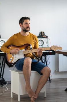 young boy with beard playing guitar at home with piano on the back