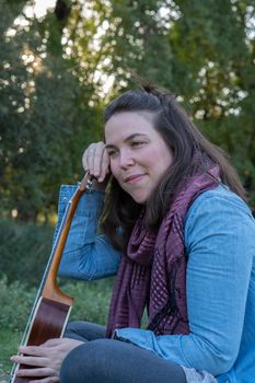 young brunette girl with long hair playing ukulele in the field on the grass