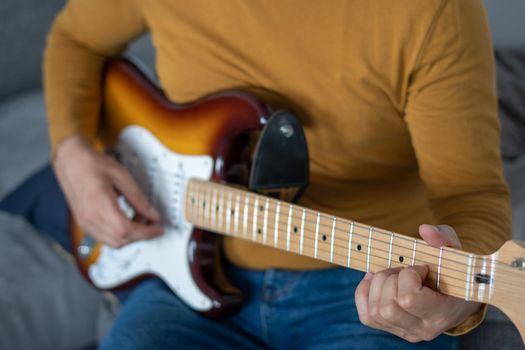 young boy with beard playing guitar at home with piano on the back