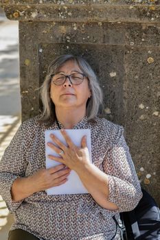 white-haired woman with glasses reading a book in the park