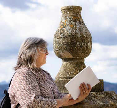 white-haired woman with glasses reading a book in the park