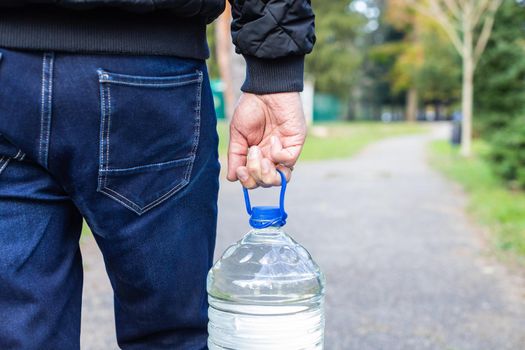 A man in jeans carries a bottle of water.