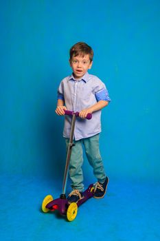 A boy on a scooter on a blue background . An article about children's scooters. An article about the choice of a scooter for a child. A happy child. Blue background and a boy. Copy Space