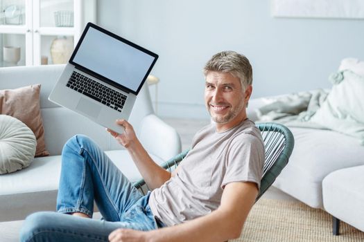 happy man sitting in a chair and showing his new laptop. side view.