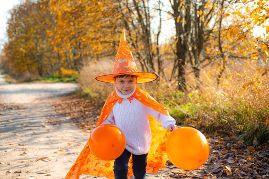 Portrait of a boy in Halloween clothes with pumpkin balloons on the street . A traditional holiday. October 31. Autumn Holiday