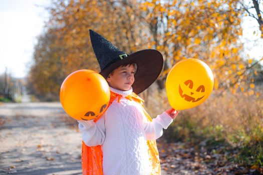 Portrait of a boy in Halloween clothes with pumpkin balloons on the street . A traditional holiday. October 31. Autumn Holiday