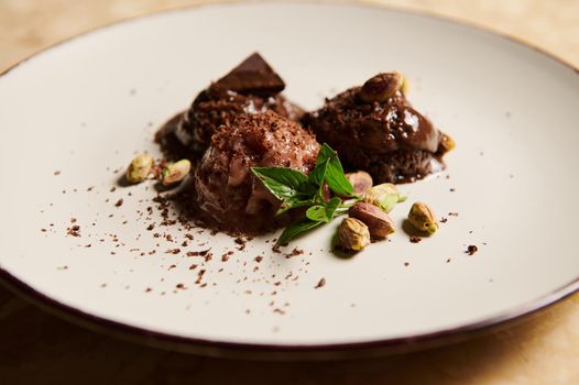 Close-up. Food still life. Frozen balls of vegan chocolate ice cream, with pistachio and lemon basil leaves, melting on white plate on marble surface. Sweet dessert for refreshment on hot summer days