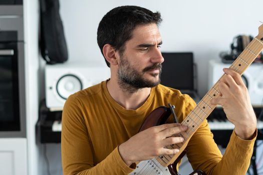 young boy with beard playing guitar at home with piano on the back