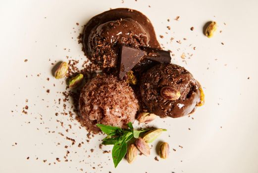 Top view. Food still life composition of dairy free, raw vegan cocoa ice cream sorbet balls, decorated with sprinkled pistachio, lemon basil leaves and dark chocolate, over white background