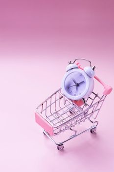 Black alarm clock and toy shopping cart isolated on white. watch in the shopping cart, lack of time, waste of time, shopping time.