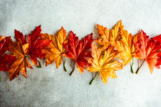 Bright red and yellow fake maple leaves on the concrete background
