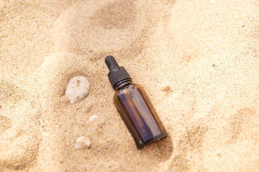 Cosmetic serum for the skin in a glass bottle. A bottle with a pipette on a sandy beach by the sea. Essences for skin care on a sandy background. The concept of natural cosmetics and SPA products.