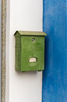 Old green mailbox on the white and blue wall of the house close up