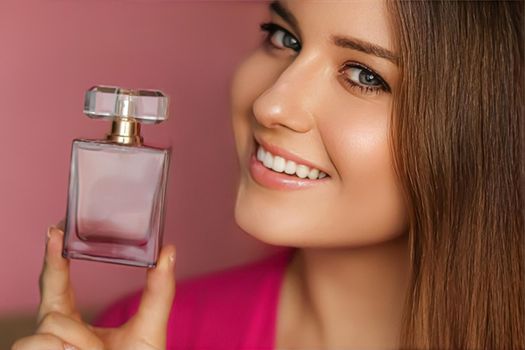 Perfume, beauty product and cosmetics model face portrait on pink background, beautiful woman holding fragrance bottle with floral feminine scent, fashion and makeup concept