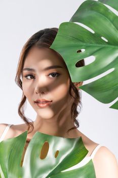 Closeup portrait of young gorgeous woman with healthy fair skin holding big green leaf near her face. Skin care beauty care concept.