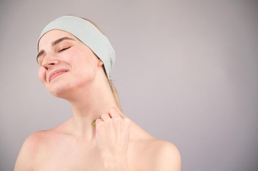 Portrait of a young woman massages her face with a gouache scraper on a white background