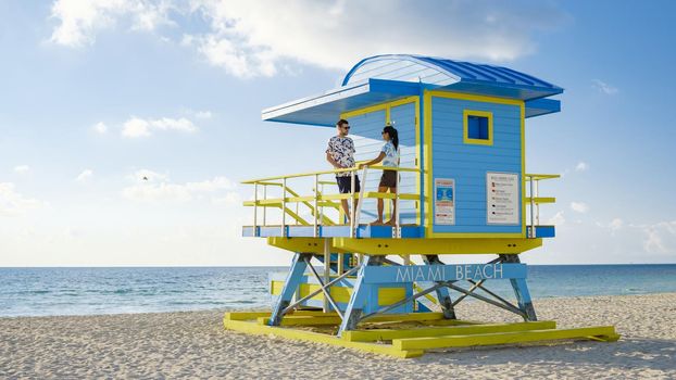 Miami Beach, a couple on the beach in Miami Florida, lifeguard hut Miami Asian women and caucasian men on the beach during sunset. man and woman relaxing at a lifeguard hut looking at ocean