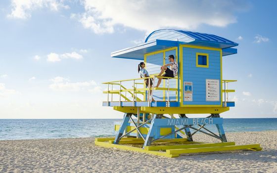 Miami Beach, a couple on the beach in Miami Florida, lifeguard hut Miami Asian women and caucasian men on the beach during sunset. man and woman relaxing at a lifeguard hut looking at ocean