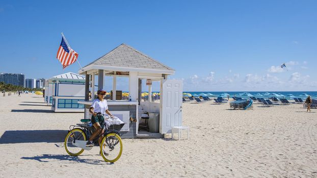 Young women on the beach Miami with a bicycle, colorful Miami beach, and a Lifeguard hut in South Beach, Florida. Asian women bicycle on the beach