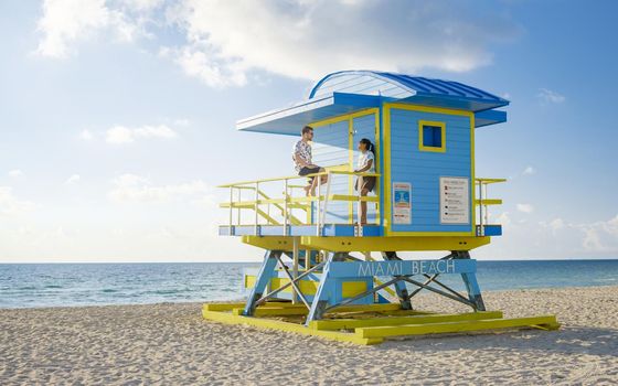 Miami Beach, a couple on the beach in Miami Florida, lifeguard hut Miami Asian women and caucasian men on the beach during sunset. man and woman relaxing at a lifeguard hut looking at ocean