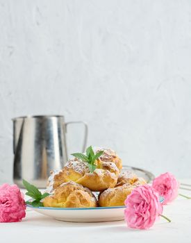 Baked eclairs with custard cream on a metal round plate sprinkled with powdered sugar