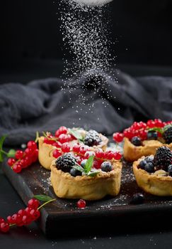 Fruit tart with red currants sprinkled with powdered sugar on a black table