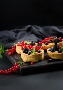 Fruit tart with red currants sprinkled with powdered sugar on a black table