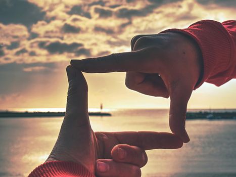 Hands making finger shape gesture, hand hold sun above stony fisherman pier, Mallorka island.