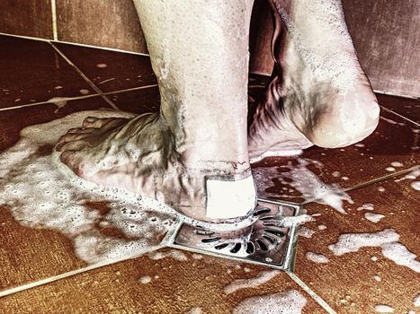 Shovering with painful skin on foot with adhesive plaster.  Female body taking shower in  tiled modern bathroom.