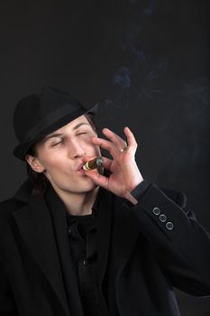 Man in black cloth and hat smoke cigar with taste