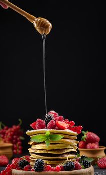 Stack of pancakes with fresh fruit sprinkled with honey on a black background