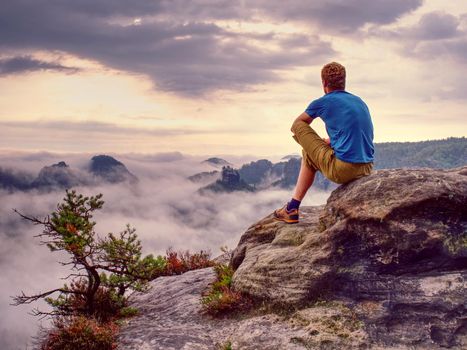 Autumnal misty morning in wild nature. Hiker in sports wearing stand on sharp peak and watching natural show in valley bellow.