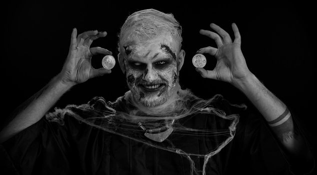 Scary man with bloody scars face, Halloween zombie showing golden bitcoins. Achievement career wealth, cryptocurrency investment, mining, future technology. Scary wounded undead guy smiles terribly