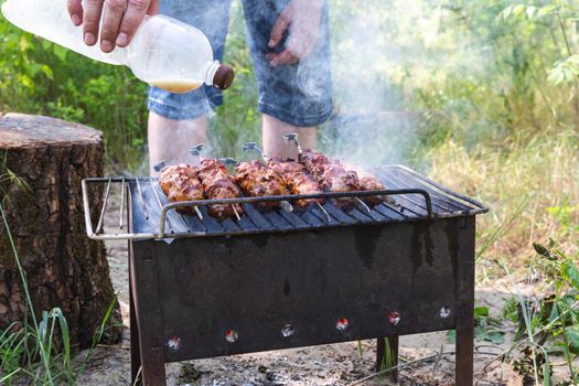 Man fries pork meat on the grill. Barbecue for a summer party. Skewers on a spit. Rest at nature.