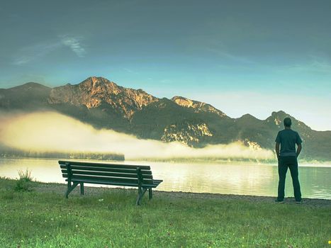 Man stay lonely at the bench in front of the lake. Tourist enjoys beautiful views of mountain lake