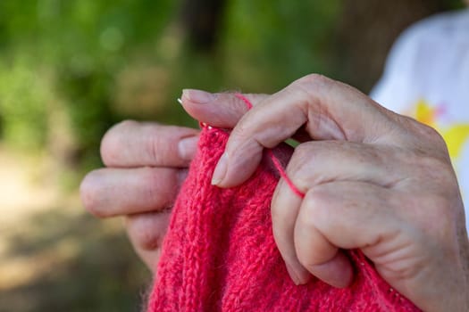 Grandmother knits woolen things with knitting needles. Hands closeup.