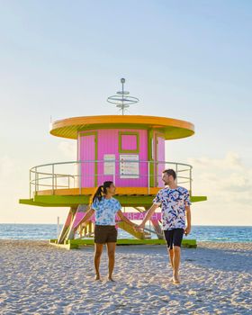 Miami Beach, a couple of men and women on the beach in Miami Florida, lifeguard hut Miami Asian women and caucasian men on the beach during sunset. man and woman relaxing at a lifeguard