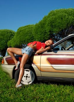 Pretty woman pin-up style lay on retro car at summer sunset