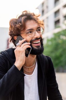 vertical portrait of a young caucasian man smiling happy while talking on his mobile phone, concept of technology of communication and urban lifestyle