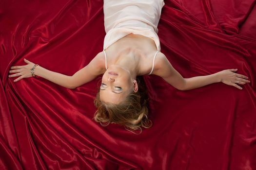 Pretty blond woman with gold hairs on red silk relax in desire