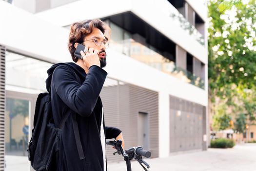 stylish young man standing with his bike talking on a mobile phone in the city, concept of urban lifestyle and sustainable mobility, copy space for text