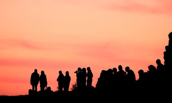 Silhouettes of people with different expressions on the embankment of the sea sunset. The crowd is watching the sunset.