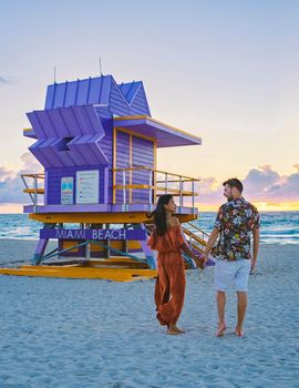 Miami Beach, a couple of men and women on the beach in Miami Florida, lifeguard hut Miami Asian women and caucasian men on the beach during sunset. man and woman relaxing at a lifeguard