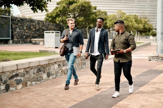 Watch out world, here we come. a group of young businesspeople chatting while walking through the city